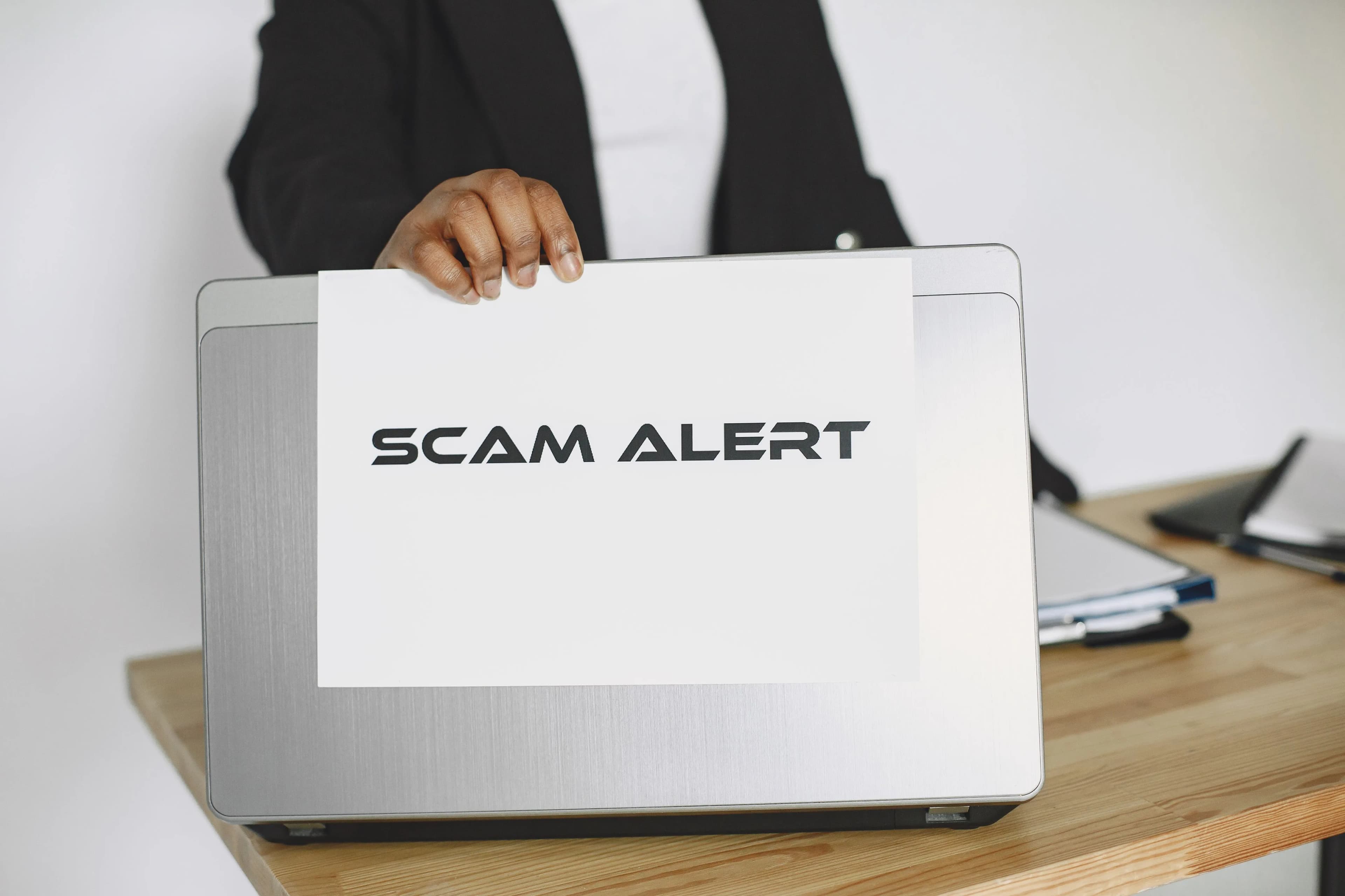 A business person holding a scam alert warning sign over a laptop