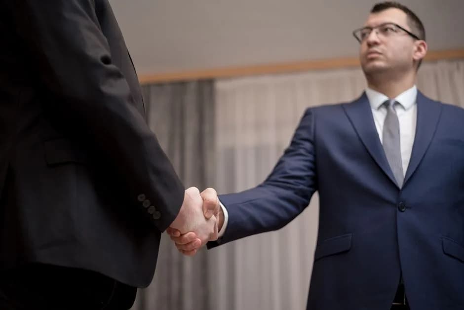 Two business people shaking hands in an office setting, representing the more than 140 companies backing the Open USD stablecoin consortium. Photo by George Morina on Pexels.