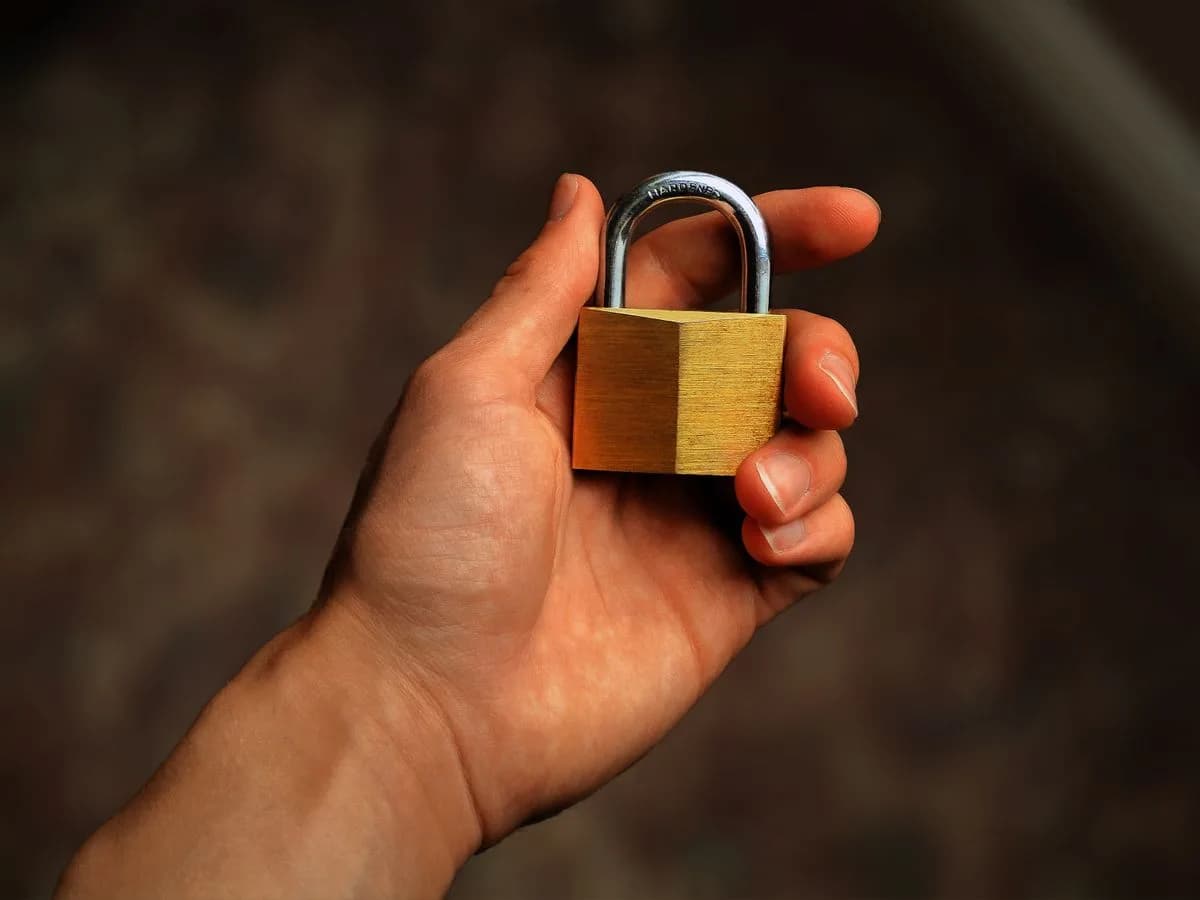 Hand holding a brass padlock, symbolizing the security model behind an onchain AI agent's approval flow. Photo by Nathan Thomas on Pexels.